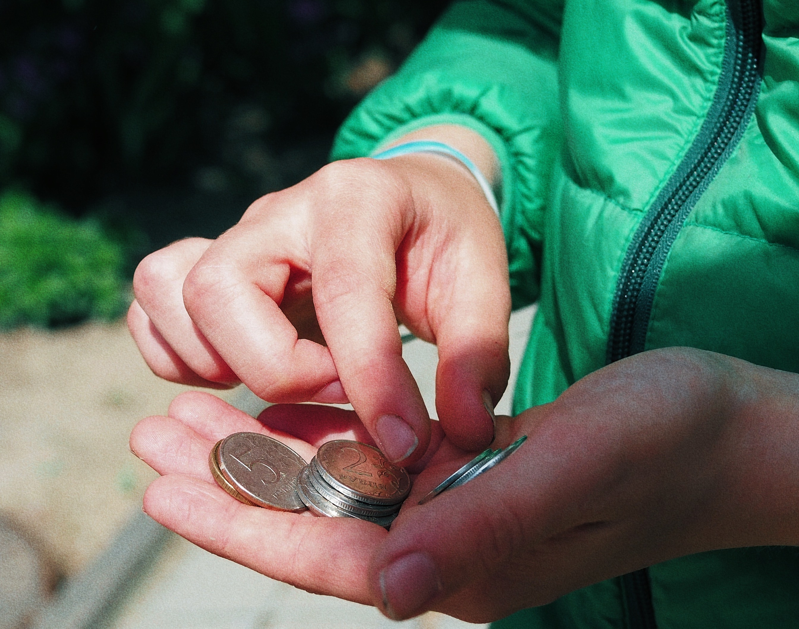 A hand holding coins with a green jacket